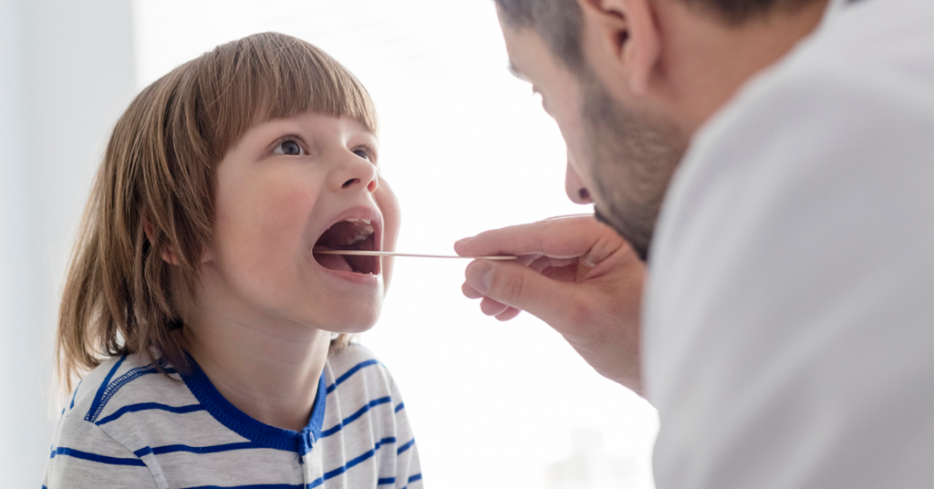 young boy being examined by an ENT physician with tongue depressor