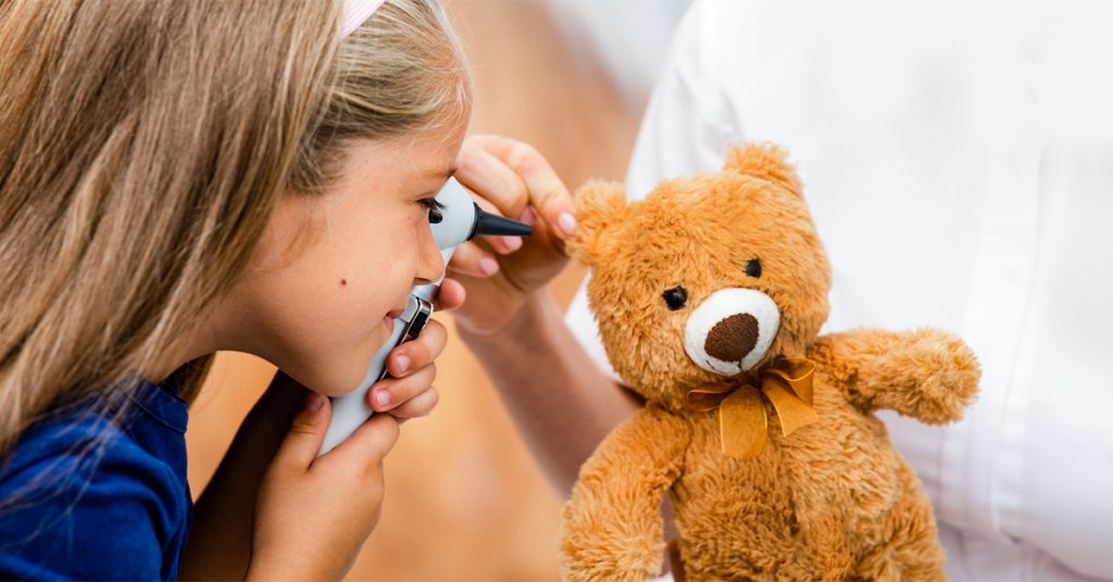 Young girl check her teddy bear's hearing