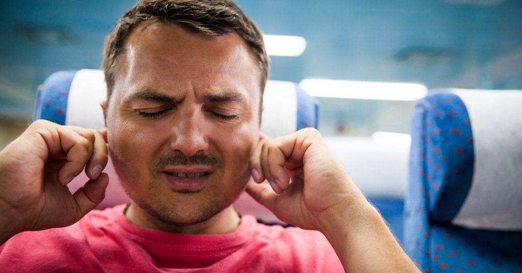 Man on an airplane holding his ears in pain